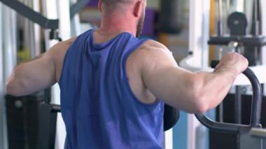 Spor salonunda bir adam çalışıyor. Sporcu bir sporcu sırt kaslarını çalıştırıyor. Arkadan görüntüle.