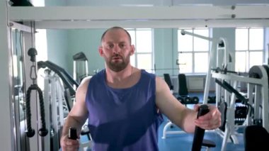 Spor salonunda eliptik bir antrenörde erkek bir sporcu. Kolları hareket ettiriyor. Spor salonu çeşitli egzersiz makineleriyle dolu..