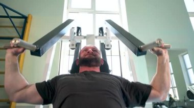 Atletik yapılı bir adam spor salonundaki bir makinede çalışıyor. Sırt ve göğüs kaslarını geliştiriyor..