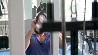 Spor salonunda ağırlık makinesi kullanan bir adam. Sporcu antrenmanına odaklanmış.