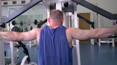 Spor salonunda ağırlık makinesi kullanan bir adam var. Kol kaslarını çalıştırıyor..