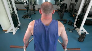 Spor salonunda ağırlık makinesi kullanan bir adam. Spor salonu temiz ve temiz, mavi ve beyaz renklerde. Arkadan bak..