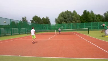 Tenis kortunda, iki genç çocuk tenis oynamayı öğreniyor..