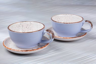 Gri arkaplanda seramik kil bardaklar ve çay tabakları.