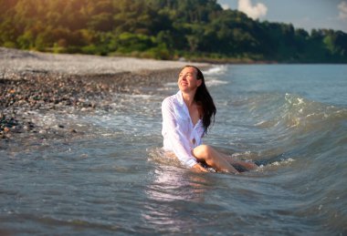 Denizde ıslak beyaz gömlekli, orta yaşlı güzel bir kadın..
