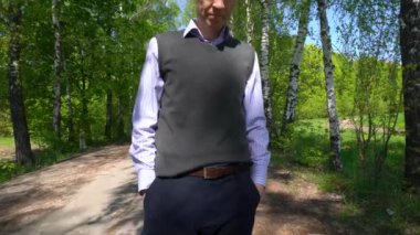 Pantolon ve siyah ayakkabı giymiş bir adamın bacakları ağaçların arasında bir futbol topunu baştan başa yuvarlıyor..