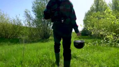 Balıkçı, elinde olta kamışı ve kova dolusu suyla gölden geriye doğru yürüyor. Kovboy şapkası, ekose gömlek, gri pantolon ve lastik çizme giyiyor. Dışarıda güneşli bir gün ve bir sürü sivrisinek var..
