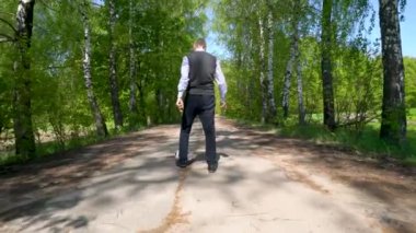 Mavi çizgili tişört ve süveter giyen yaşlı bir adam, siyah pantolon ve siyah çizmeler giymiş, huş ağacından bir sokakta bir futbol topuyla oynuyor..