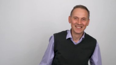 Yaşlı, zayıf bir adam gri bir arka planda poz veriyor, neşe ve ifade gösteriyor..