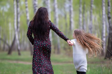 Anne ve kızı sırtları kameraya dönük bahar ormanlarında yürüyorlar..