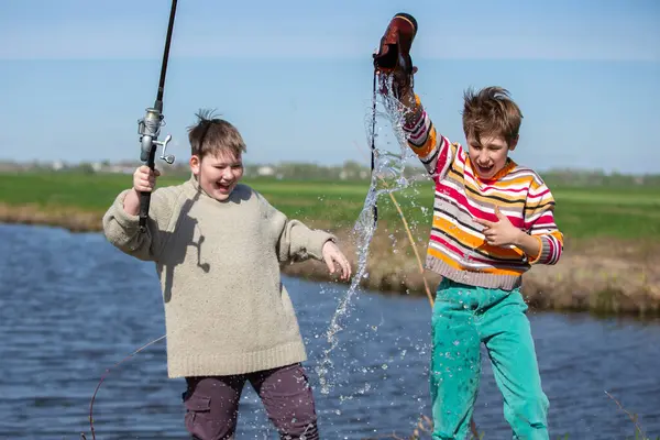Balık tutmak eğlenceli. Çocuğun iki arkadaşı eski bir ayakkabıyı oltayla yakalamış ve gülüyorlar..