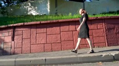 Siyah elbiseli bir kadın güneşli bir yaz gününde asfalt yolda yürür. Aşağı iniyor..