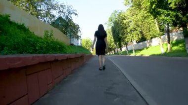 Siyahlı bir kadın taşralı bir yaz kasabasının caddesinde yürüyor. Arkadan görüntüle.