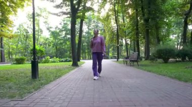 Günlük giysiler içinde yetişkin bir kadın park alanında yürüyor. Elinde bir telefon tutuyor..