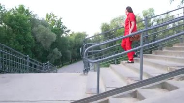 Kırmızı elbiseli orta yaşlı bir kadın şehir merdivenlerinden sete iniyor..
