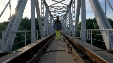 Orta yaşlı bir kadın güneşli bir yaz gününde demiryolu köprüsünden geçer..