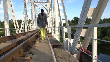 Güneşli bir yaz gününde orta yaşlı bir kadın demiryolu köprüsünden geçer. Sarı pantolon ve gri bir bluz giyiyor..