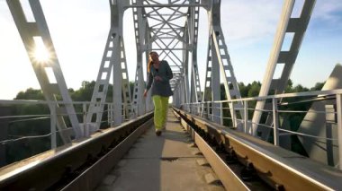 Orta yaşlı bir kadın güneşli bir yaz gününde tren yolu köprüsünden geçer..