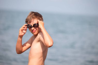 Denizin arka planında yüzme gözlüklü küçük bir çocuk..