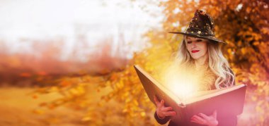 Cadılar Bayramı 'nda büyücü şapkalı bir kadın ormanın sonbahar arka planında büyü yapıyor..