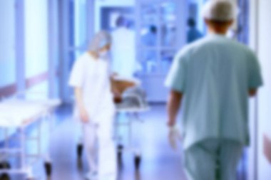 Mavi renkli hastalar ve doktorların olduğu bulanık bir hastane koridoru..