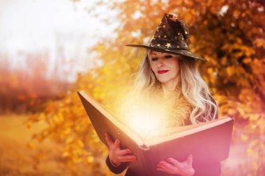 Cadılar Bayramı 'nda büyücü şapkalı bir kadın ormanın sonbahar arka planında büyü yapıyor..