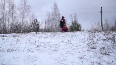 Çocuklar neşeyle karlı bir yamaçtan aşağı kayıyor.