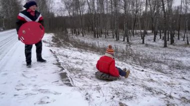 Çocuklar karlı bir yamaçtan kayarken eğleniyor..