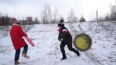 Çocuklar karlı bir tepeden kayıyor.
