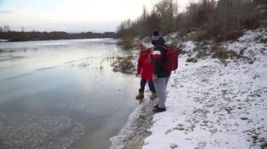 Çocuklar nehir kıyısındaki kış manzarasının tadını çıkarıyorlar..