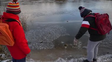 Çocuklar nehir kıyısında buzu ve suyu inceliyor..
