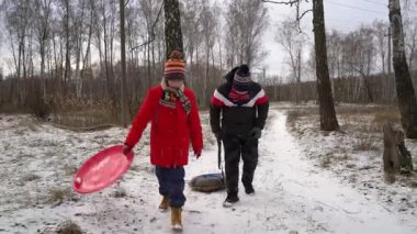 Çocuklar karlı bir ormanda birlikte yürürler..