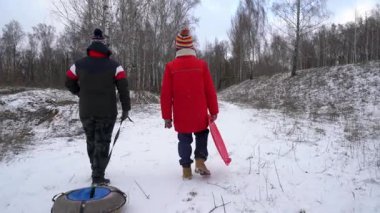 Arkadaşlar kızaklarla karlı bir ormanda yürür..