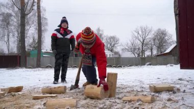 İki çocuk karlı bahçede odun kesiyor..