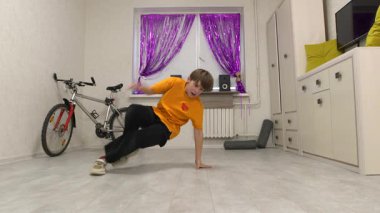 Bir çocuk, mor perdeler ve rahat mobilyalarla süslenmiş modern bir odada enerjik dans yetenekleri sergiliyor. Bisiklet hayat dolu atmosfere eşsiz bir dokunuş ekler..