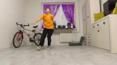 Genç bir çocuk dans figürlerini canlı perdelerle süslenmiş iyi ışıklandırılmış bir odada sergiliyor. Yaratıcılık ve neşeyi harmanlayarak kendine güvenerek hareket ederken atmosfer hayat dolu..