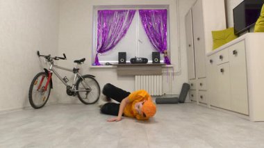 Bir dansçı hareketlerini canlı bir odada, pürüzsüz bir zeminde yapar. Renkli dekorasyonlar canlı atmosferi geliştirir, eğitim için eğlenceli bir ortam yaratır..