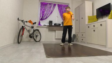 Genç bir dansçı mor perdelerle süslenmiş parlak bir odada hareket eder. Yakınlarda bir bisiklet ve ses sistemi var, enerjik bir atmosfer yaratıyorlar..