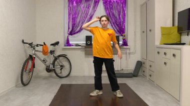 Genç bir dansçı mor perdelerle süslenmiş parlak bir odada hareket eder. Yakınlarda bir bisiklet ve ses sistemi var, enerjik bir atmosfer yaratıyorlar..