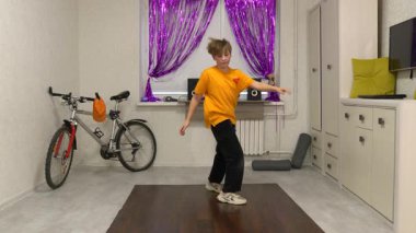 Genç bir dansçı mor perdelerle süslenmiş parlak bir odada hareket eder. Yakınlarda bir bisiklet ve ses sistemi var, enerjik bir atmosfer yaratıyorlar..