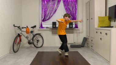 Genç bir dansçı mor perdelerle süslenmiş parlak bir odada hareket eder. Yakınlarda bir bisiklet ve ses sistemi var, enerjik bir atmosfer yaratıyorlar..