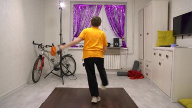 Genç dansçılar, mor perdelerle süslenmiş canlı bir odada dans ediyorlar. Antrenman için canlı bir atmosfer oluşturan bisiklet ve spor malzemeleri görülebilir..