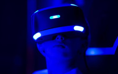 Mavi sanal gerçeklik kulaklığı takan biri. O kişi kameraya bakıyor. Sanal dünyaya girmeye hazırlanan kişinin heyecan ve beklenti anlayışı