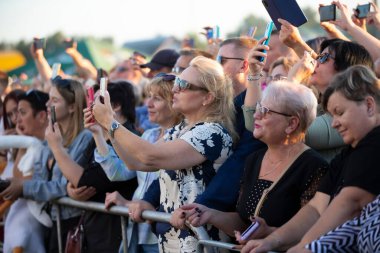 29 Temmuz 2023. Belarus, Lyaskovichi köyü. Ulusal kültürlerin kutlaması. Açık hava konserindeki izleyiciler akıllı telefonlardan neler olduğunu kaydediyor..