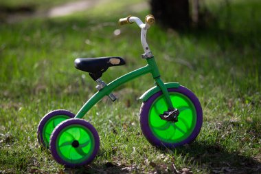 Mor tekerlekleri olan yeşil bir bisiklet çimlerin üzerinde oturur. Üç tekerlekli bisiklet eski ve eski bir görünüşü var.