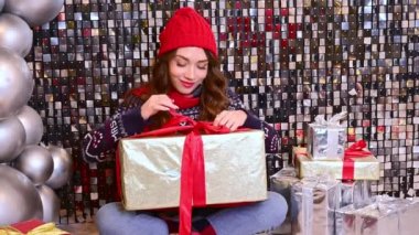 Kırmızı şapkalı güzel bir kadın, büyük bir hediyeyle eşarp yere oturur, hediyeyi büyük taşaklı parlak bir arka planda faiziyle açar..