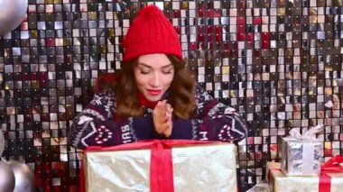 Kırmızı şapkalı güzel bir kadın, büyük bir hediyeyle eşarp yerde oturur ve büyük balonlarla ışıl ışıl bir arka planda sevinir..