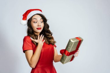 Bir kadın beklenmedik bir hediyeyle şok olur. Beyaz bir arka planı olan Noel şapkalı güzel bir esmer..