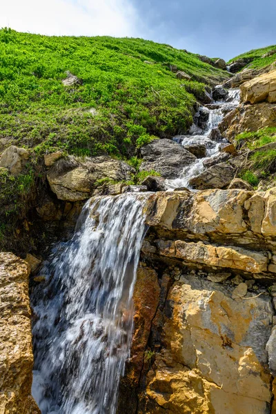 Dağlarda şelalesi olan bir dağ deresi. Dağları olan güzel bir manzara, yeşil çimenli çayırlar ve ilkbaharda yürüyüş yolu..