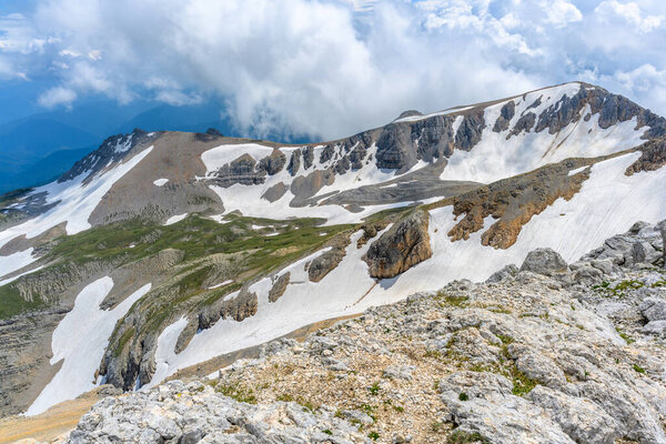 Живописный панорамный вид на идиллические холмистые пейзажи с цветущими лугами и заснеженными альпийскими вершинами. Прекрасный солнечный день с голубым небом и облаками весной.
